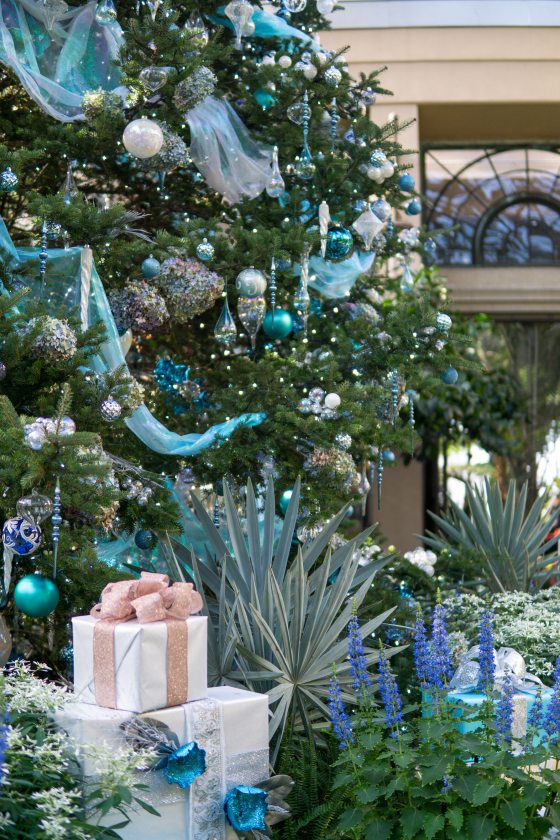 a tree decorated in blue and silver ornaments with gifts placed below it